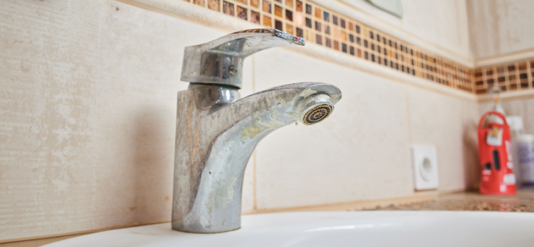 Close up of a corroded bathroom faucet with mineral buildup requiring professional plumbing repair.