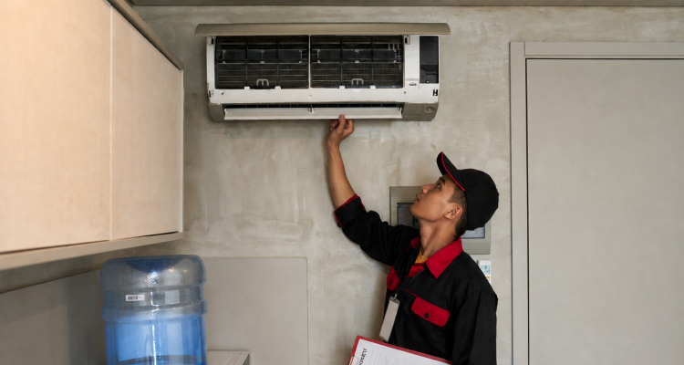 HVAC technician in a black and red uniform inspecting an open ductless mini-split air conditioner unit for home climate control in Calgary.